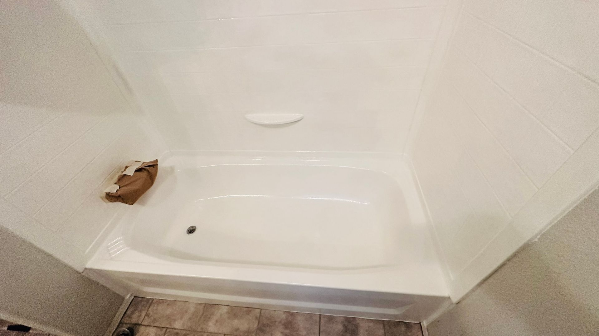 White bathtub and shower enclosure. A bar of soap rests in the center, a brown bag sits in the corner.