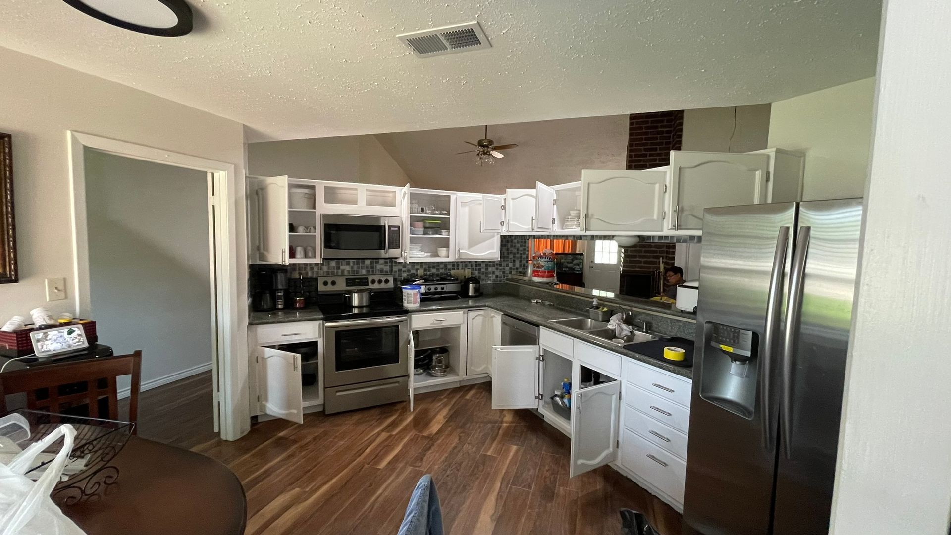 Kitchen with white cabinets, stainless steel appliances, and wood flooring; cabinets open.
