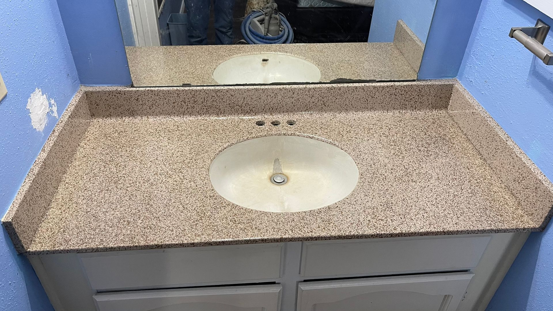 Bathroom vanity with light brown speckled countertop, white sink, and blue walls.