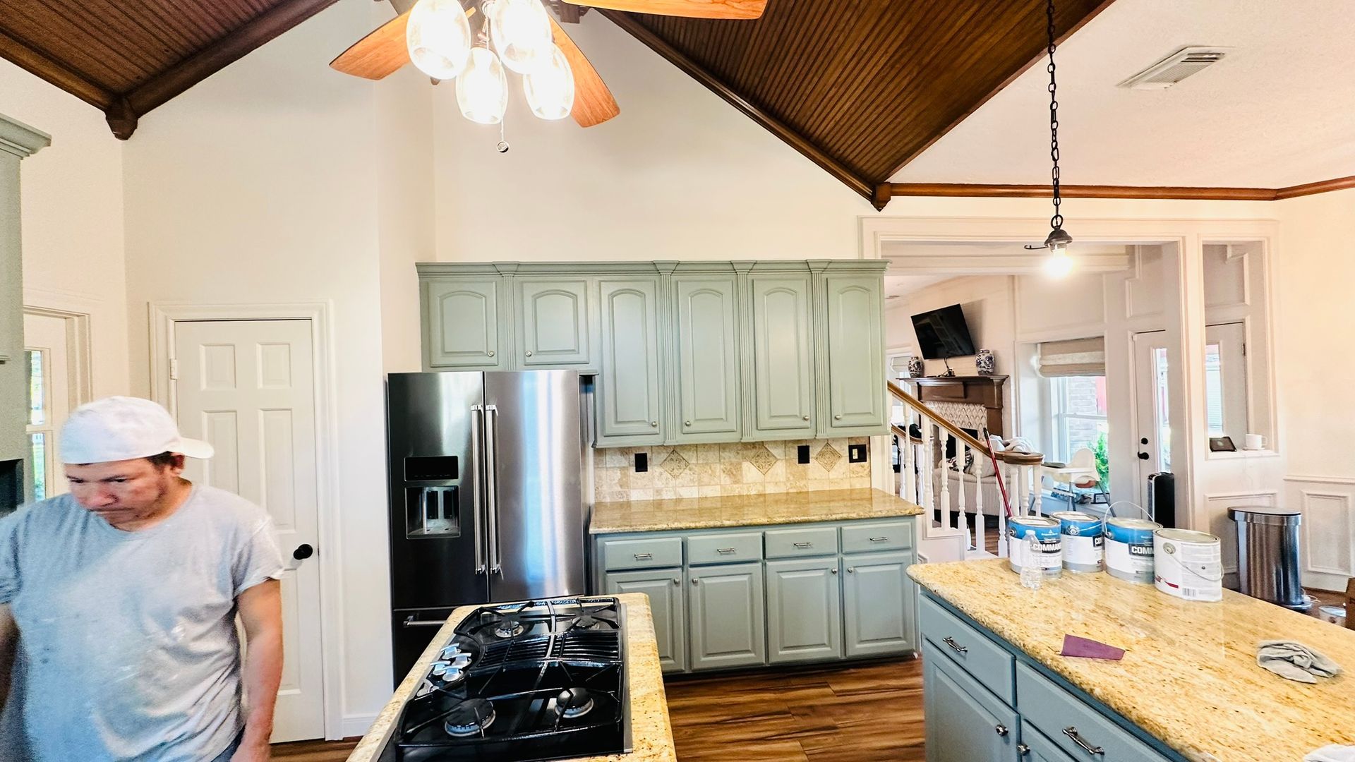 Kitchen with light blue cabinets, island with granite counter, person near a cooktop.