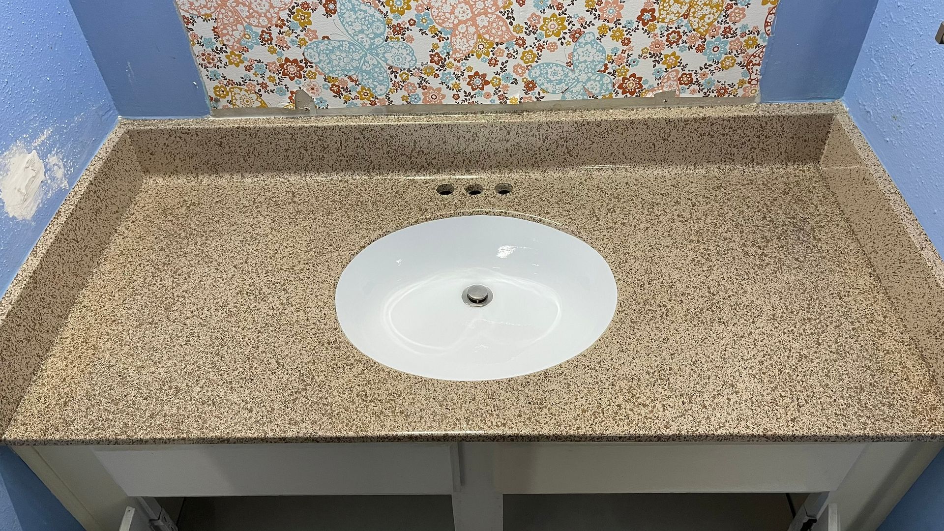 Bathroom vanity with speckled beige countertop, oval sink, and floral wallpaper.