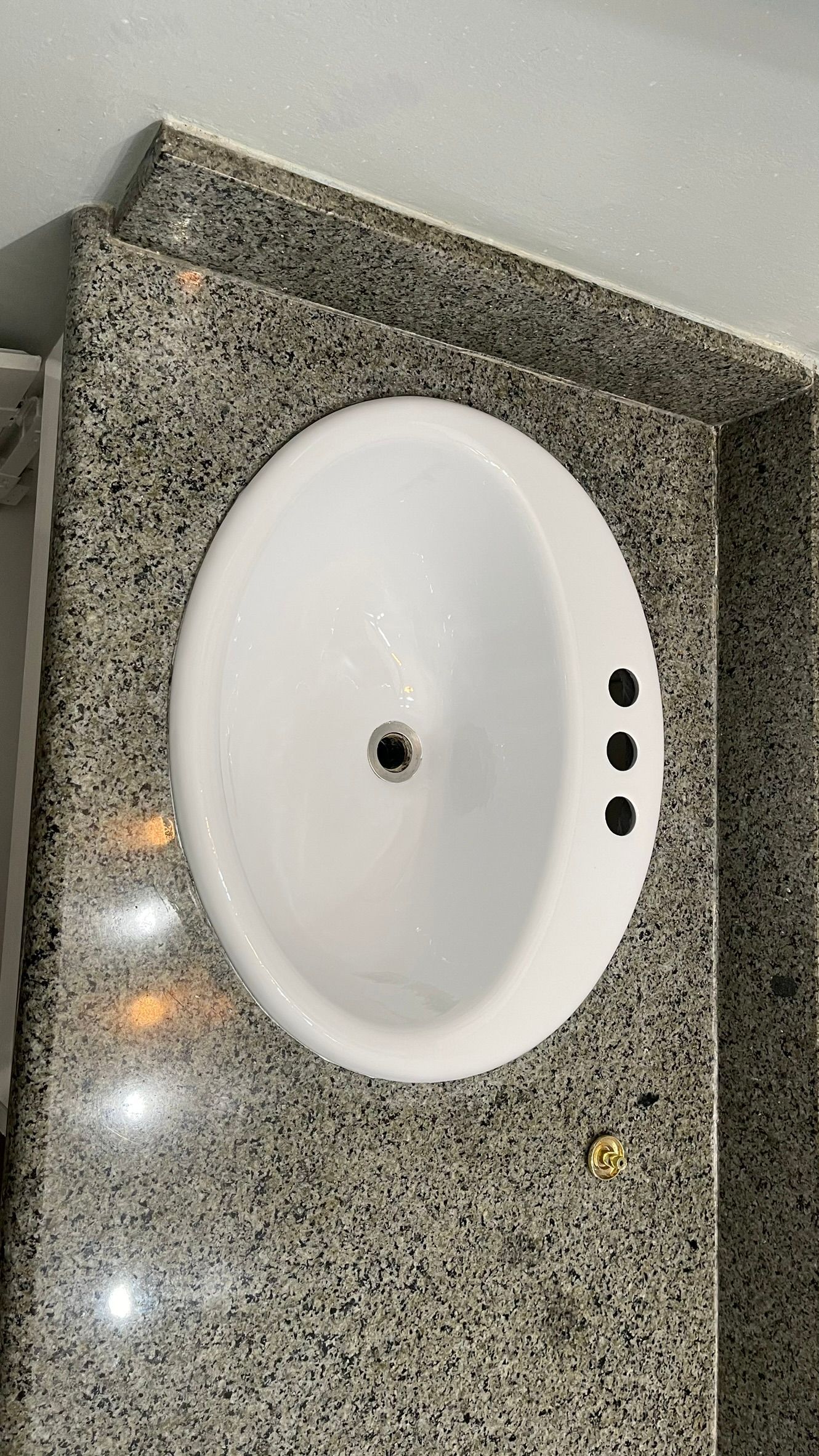White oval bathroom sink set in granite countertop. Three faucet holes are visible.
