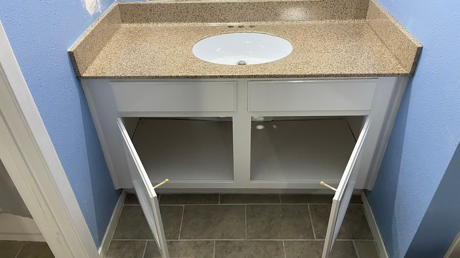 Bathroom vanity with open white cabinet doors, tan countertop, and round sink basin.