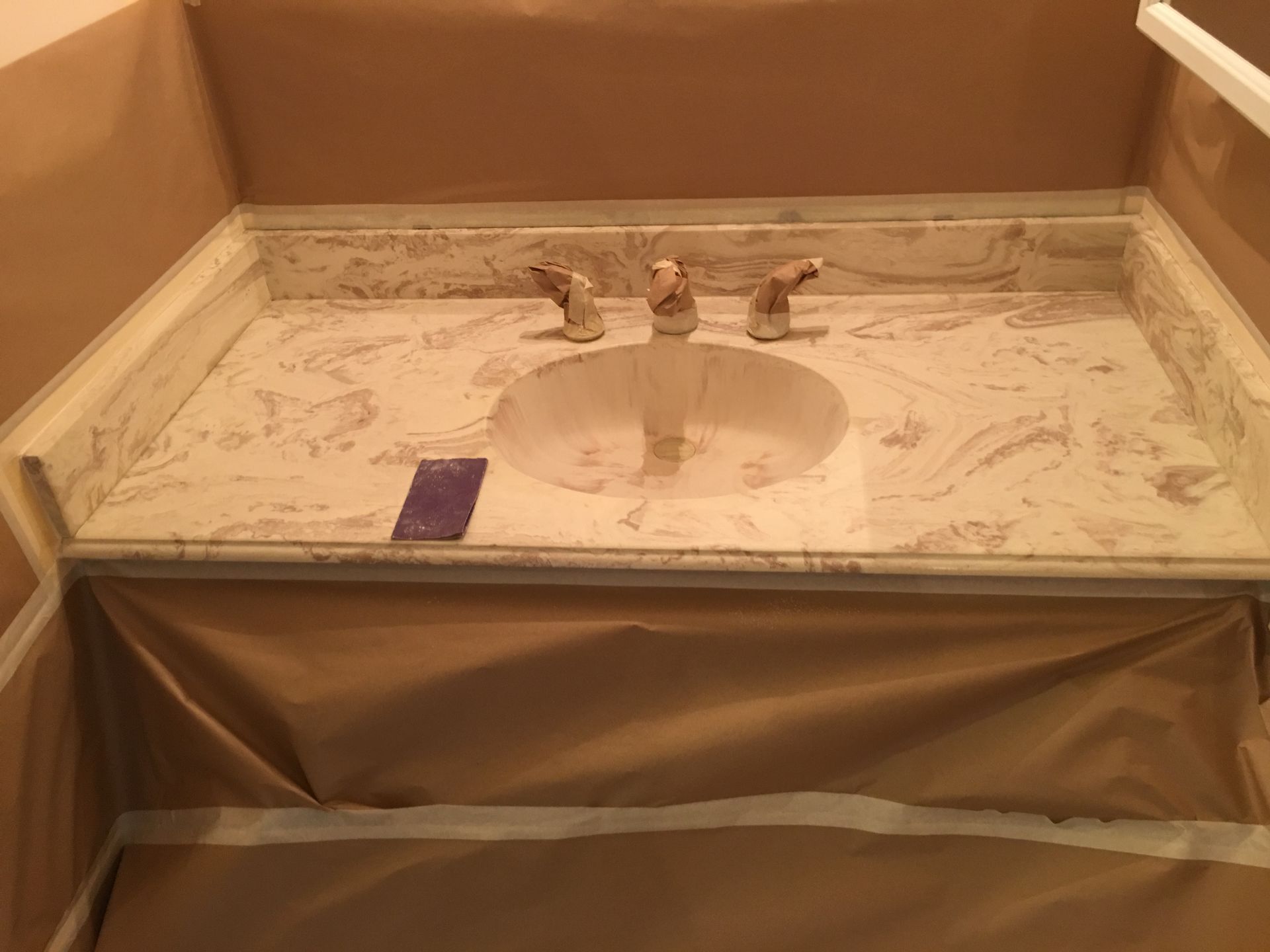 Bathroom vanity with marble countertop and oval sink, faucet. Covered in paper for protection.