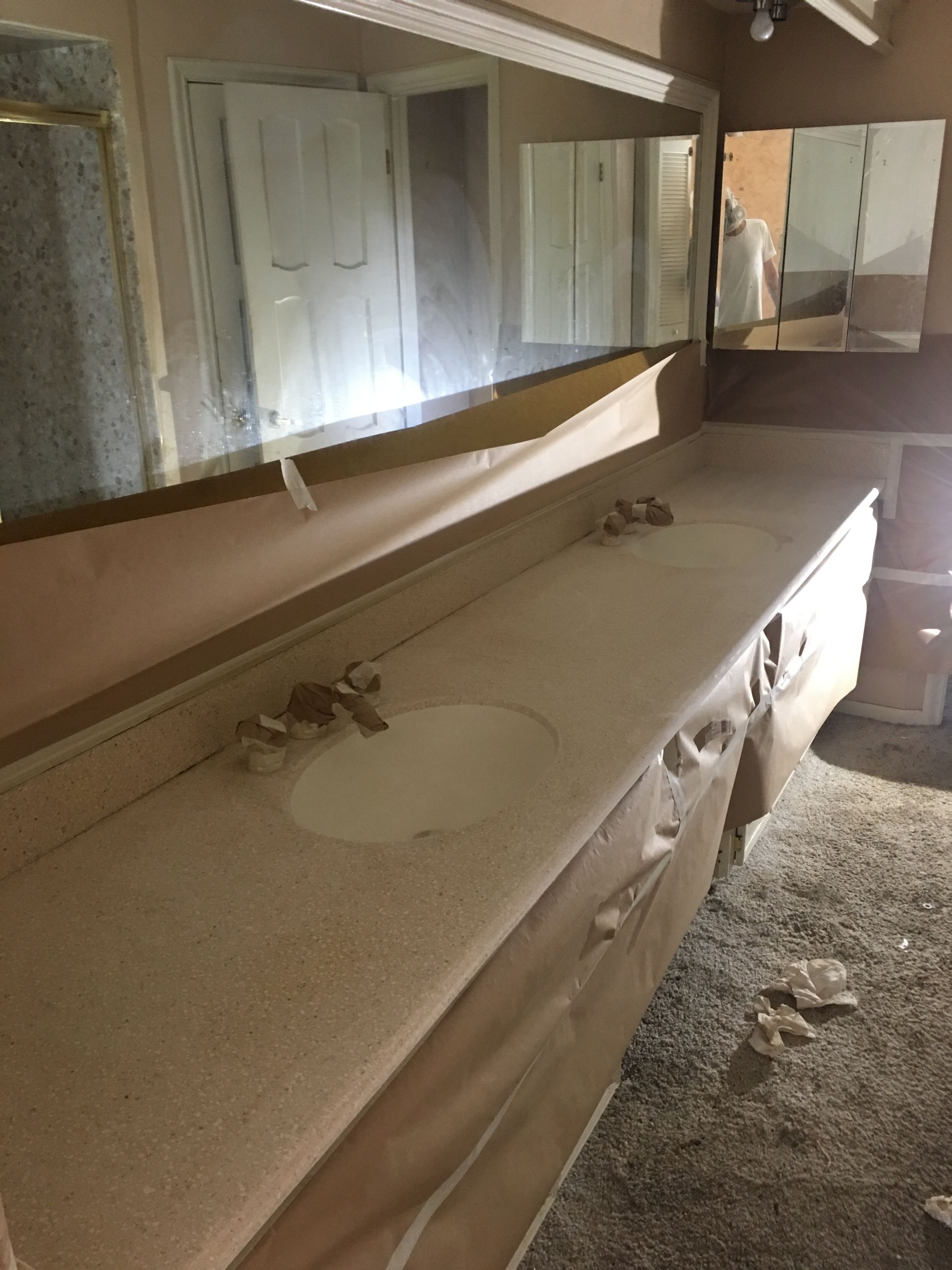Bathroom vanity with sink and faucet, covered in paper. Large mirror and cabinet visible.