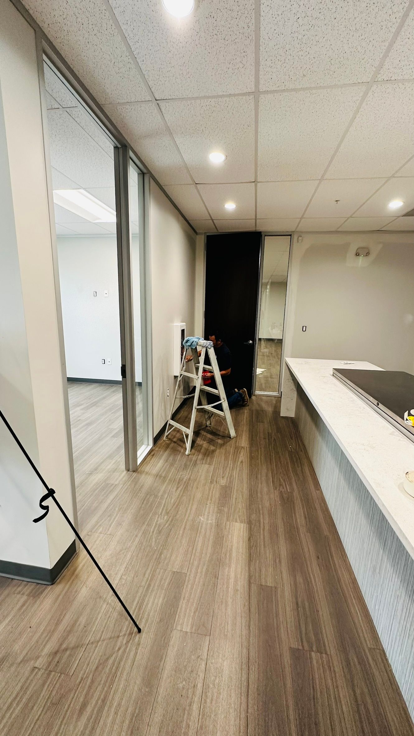 Office hallway with light wood flooring, glass walls, and a step ladder.