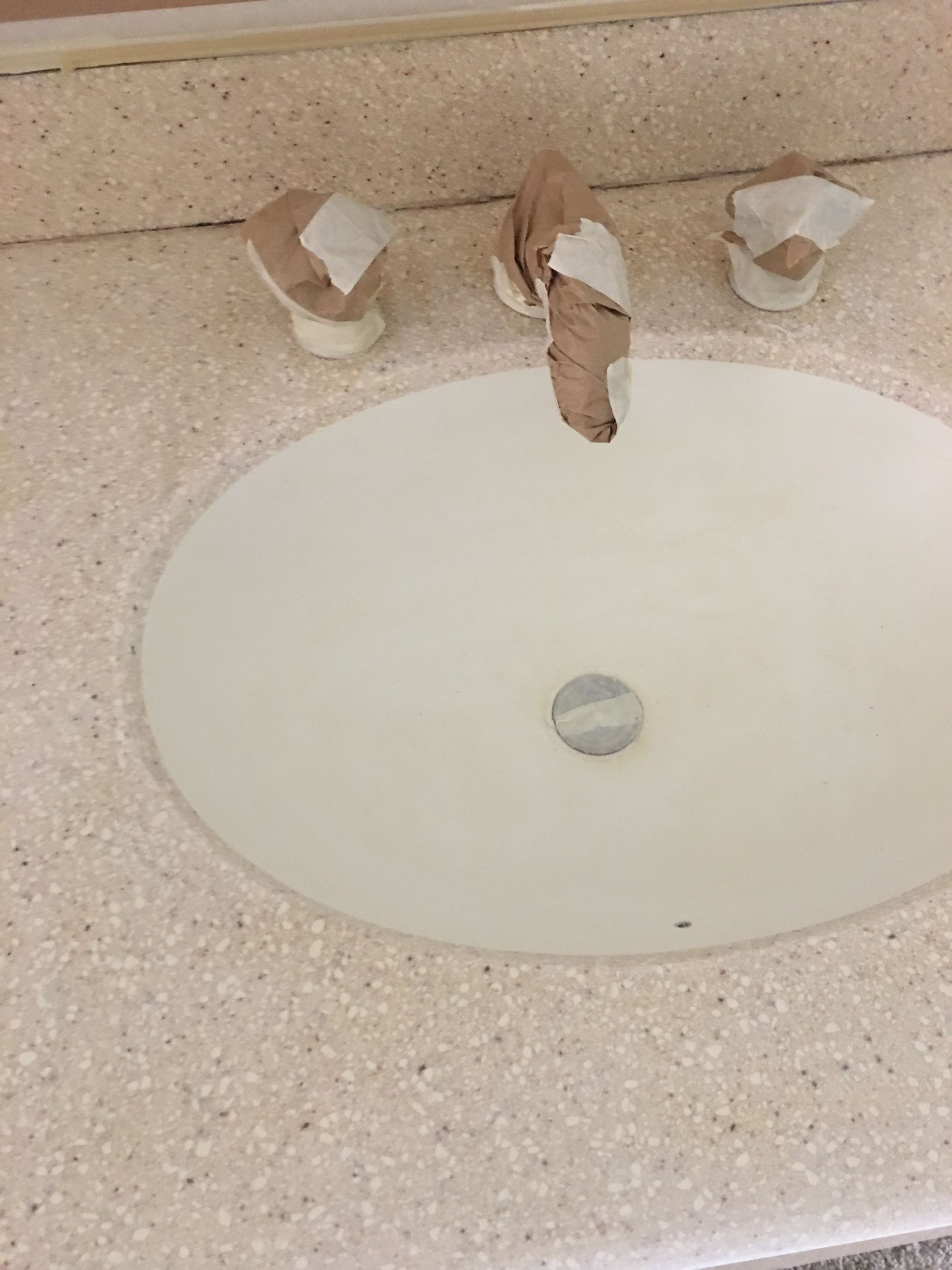 A bathroom sink with faucet and handles wrapped in brown paper, set in a speckled countertop.