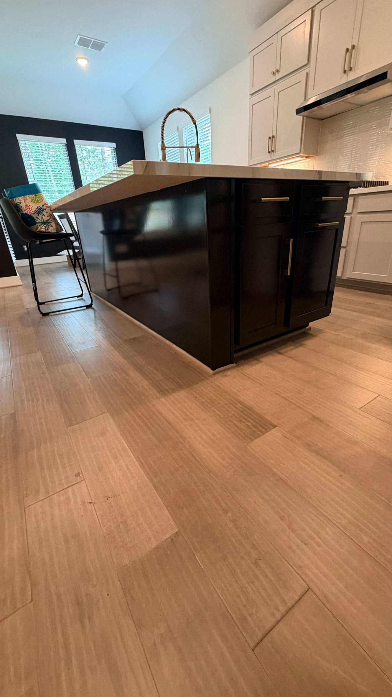 Person's hand on new dark wood floor, two workers installing flooring in background.