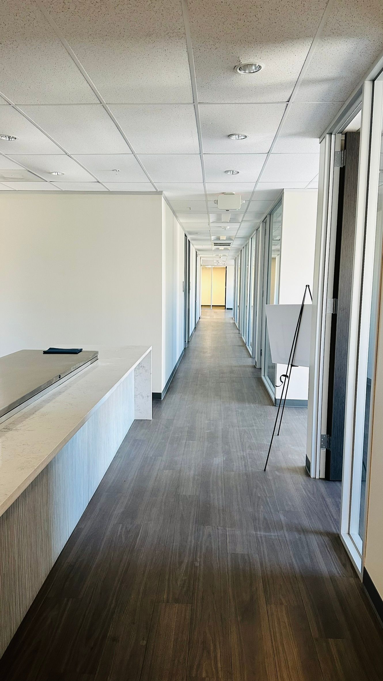 Long hallway with light-colored walls and dark carpet. Doors line the sides, and a desk is visible on the left.