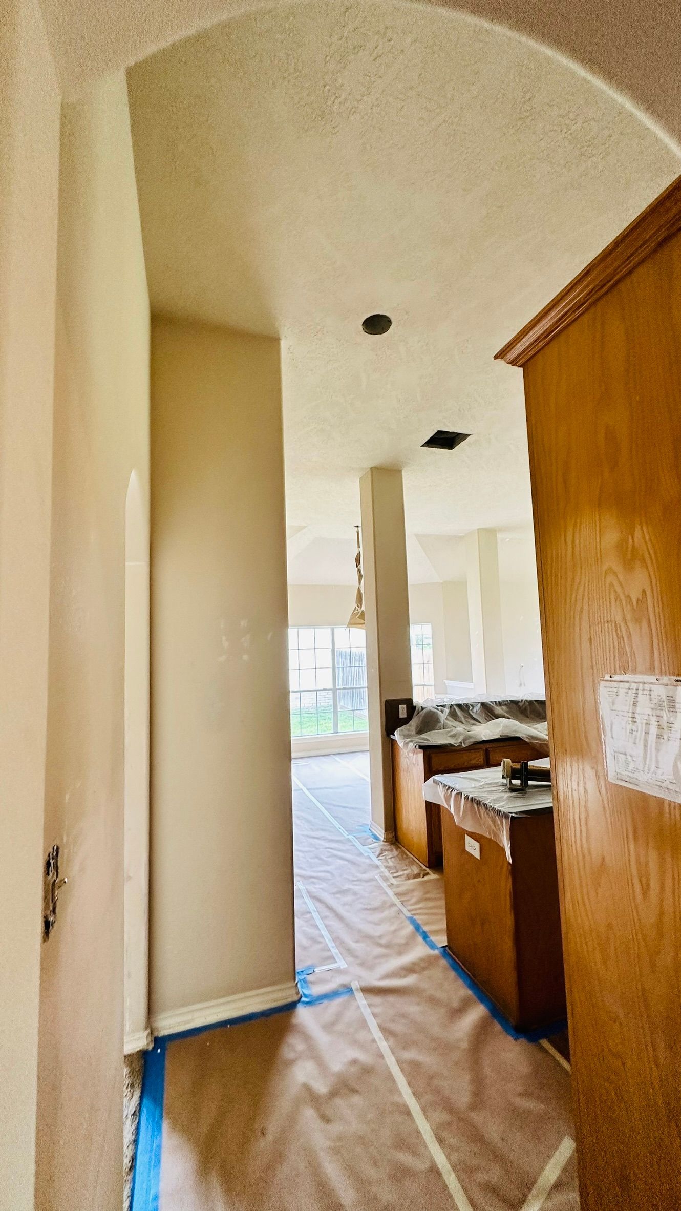 Hallway leading to kitchen, wood cabinets, plastic drop cloths, archway.