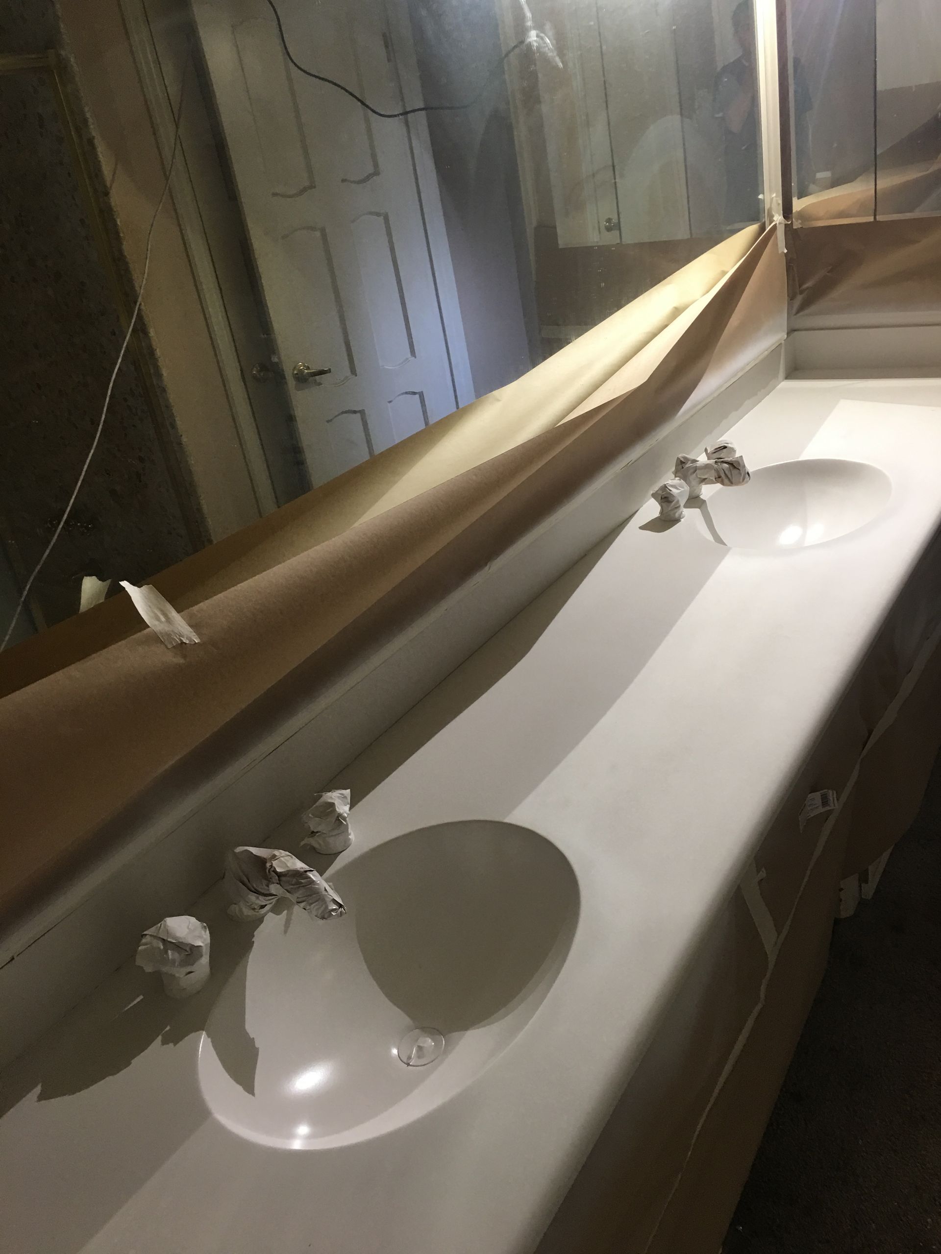 White double sink with faucets, large mirror, and visible door in a bathroom.