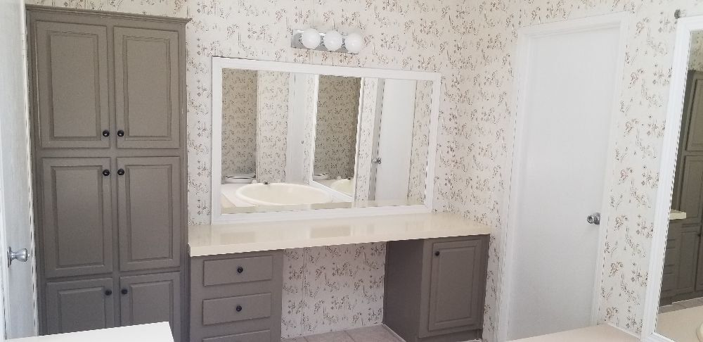Bathroom with grey cabinetry, vanity, and floral patterned wallpaper.