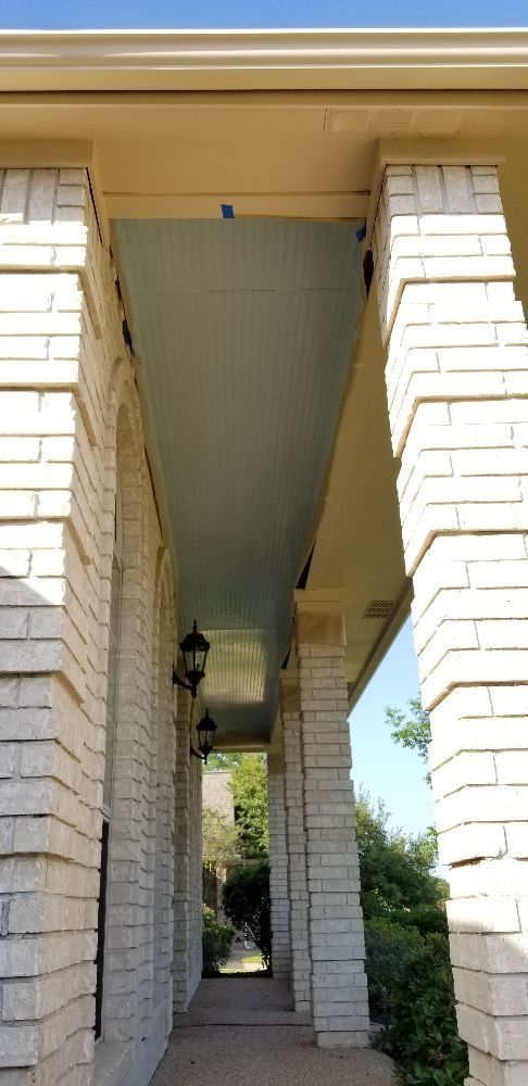 View of a covered porch with brick columns, a light-colored ceiling, and two hanging lamps.