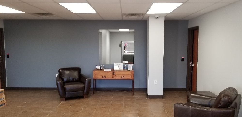 Office waiting area with two brown chairs, a wooden table, and a mirror. Gray and white walls.