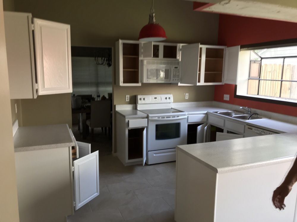 White kitchen cabinets with open doors, stove, microwave, and red accent wall.