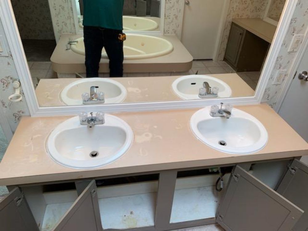 Bathroom with double sinks, a bathtub, and open cabinet doors. Light-colored countertops and walls.