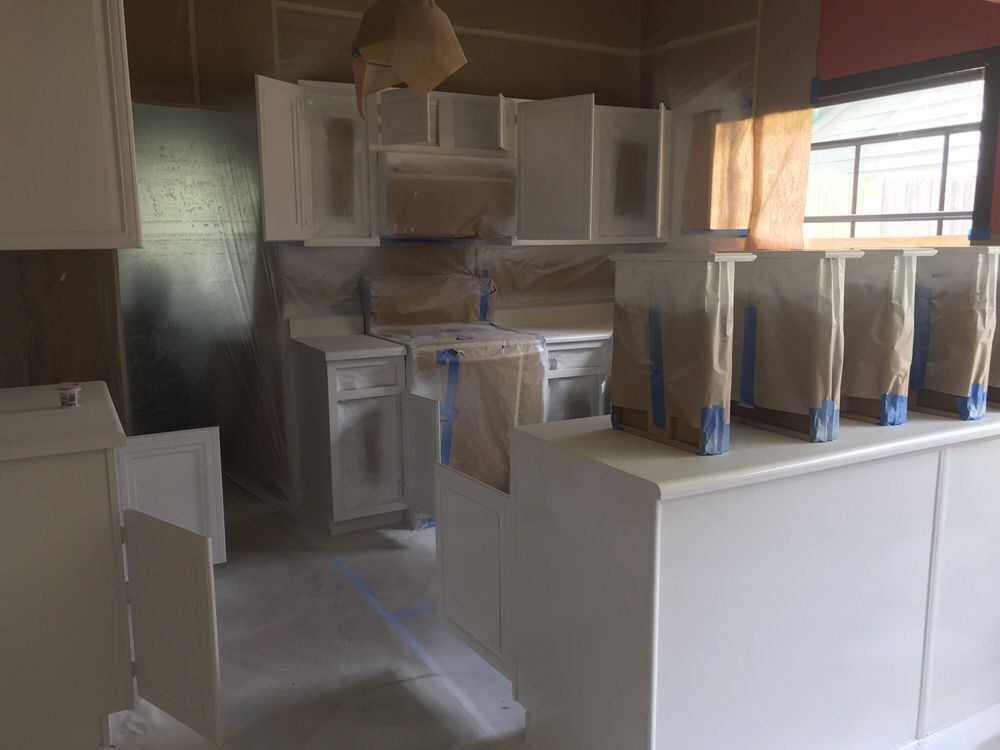 Kitchen cabinets being painted white; room protected with paper and tape.
