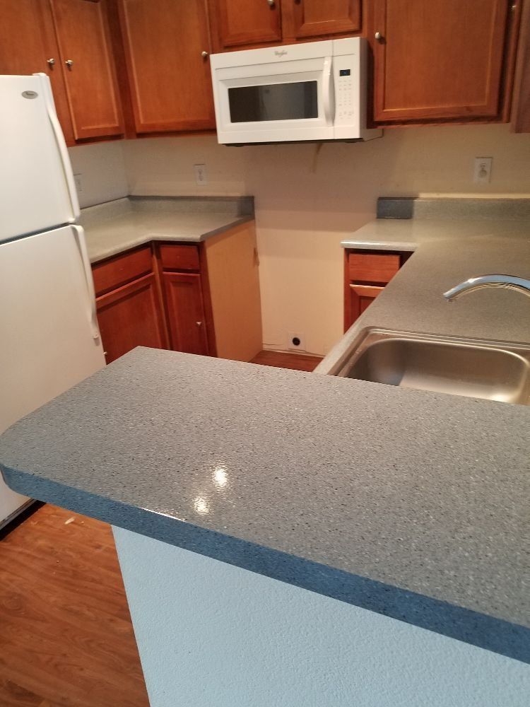 Kitchen with brown cabinets, white microwave and refrigerator, and gray countertops.
