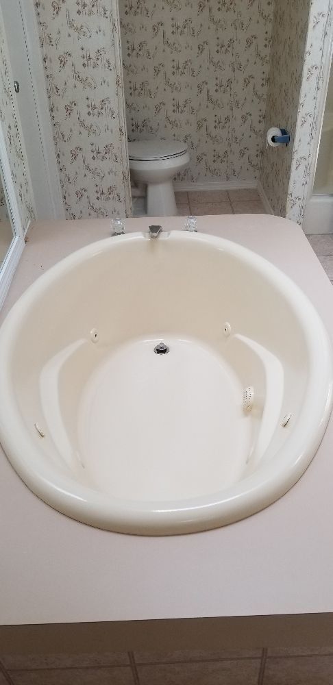 An oval, cream-colored bathtub in a bathroom with patterned wallpaper. A toilet is visible in the background.