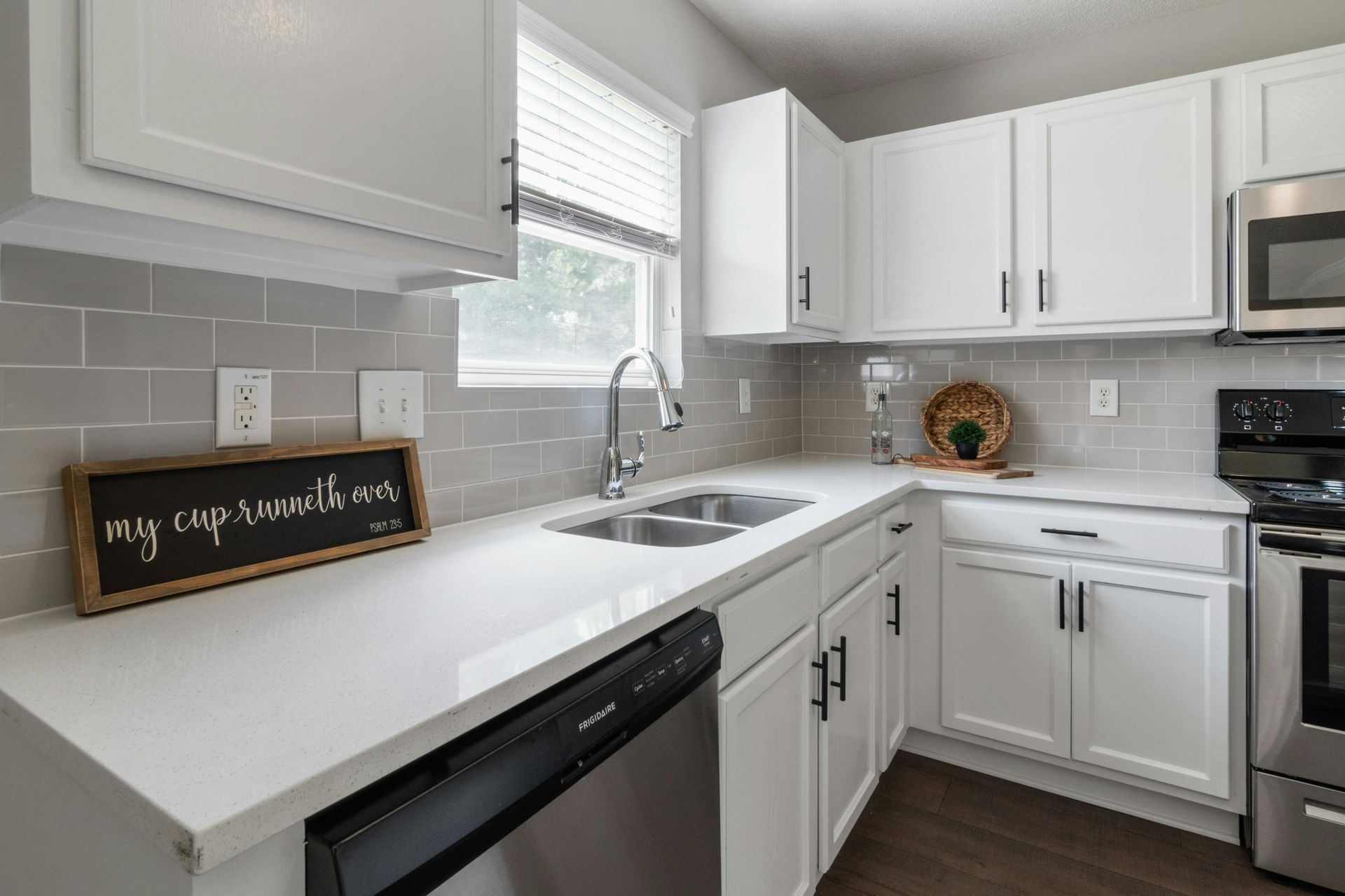 Modern white kitchen with stainless steel appliances, white countertops, and gray backsplash.