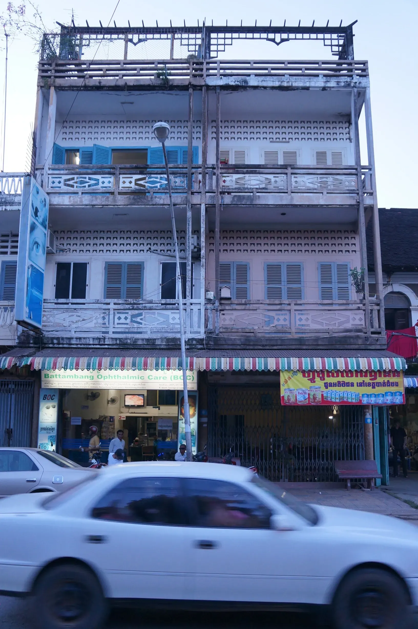 A white car is driving down a street in front of an old building