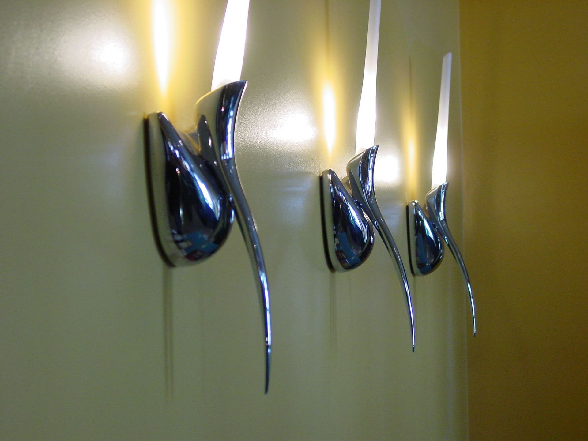 A row of chrome wall lights on a yellow wall