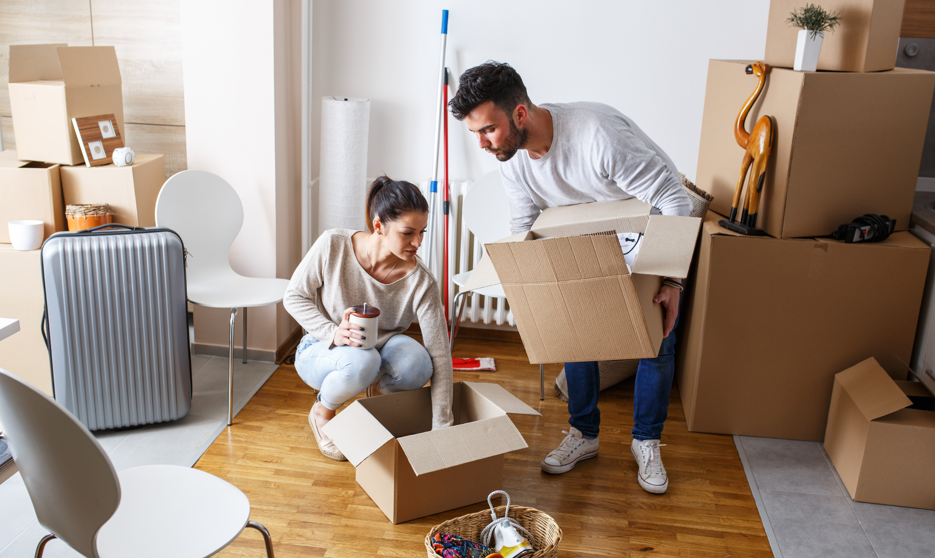 A couple unpacking cardboard boxes in their new home, surrounded by moving supplies and packed containers.