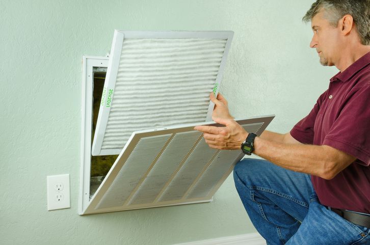 Homeowner replacing dirty HVAC air filter in wall return air vent at home.
