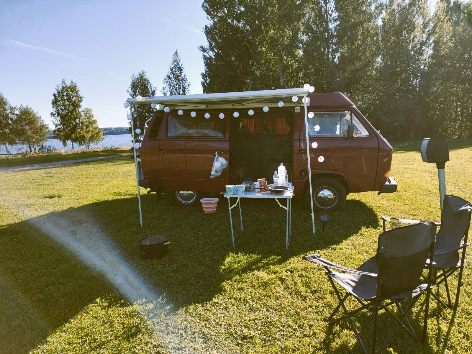 A red van is parked in a grassy field with a table and chairs