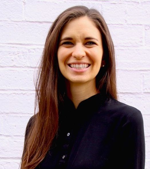 a woman in a black shirt is smiling in front of a white brick wall .
