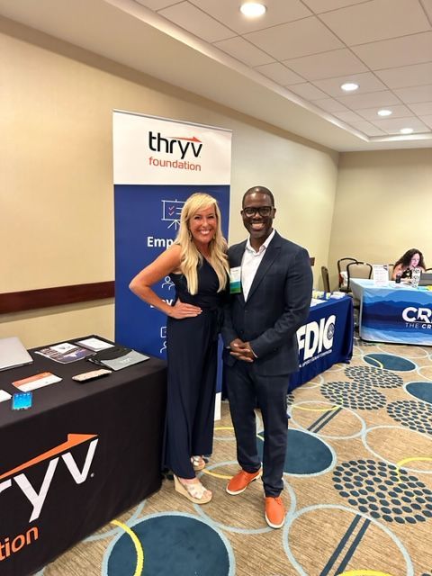 A man and a woman standing in front of a sign — Thryv Foundation