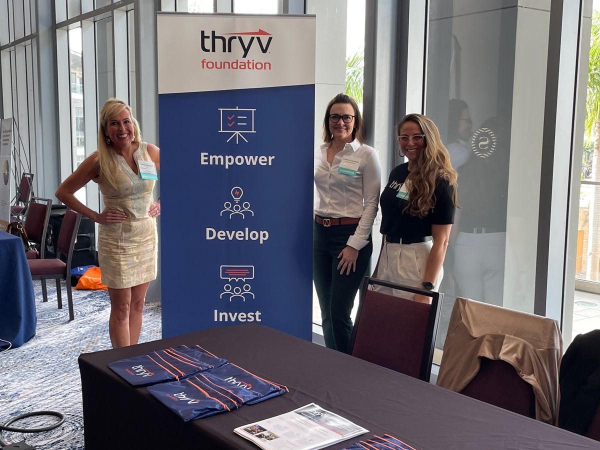A group of women standing in front of a sign — Thryv Foundation