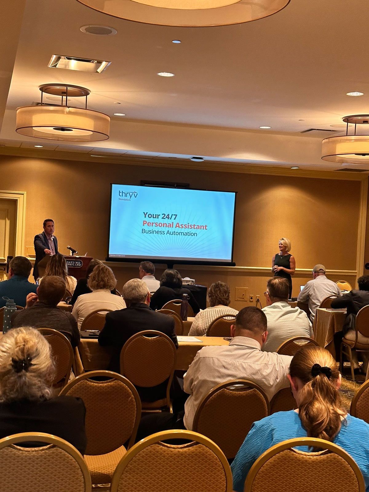 A man and a woman talking in front of a group of people — Thryv Foundation
