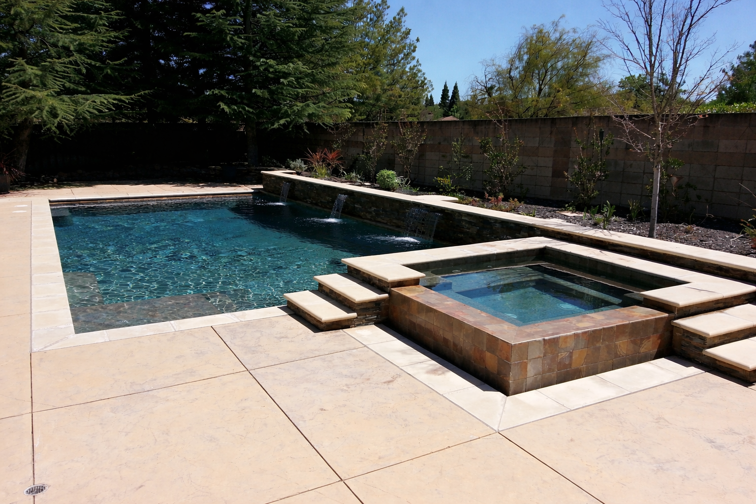 Backyard pool with a raised hot tub, stone patio, and trees along the fence