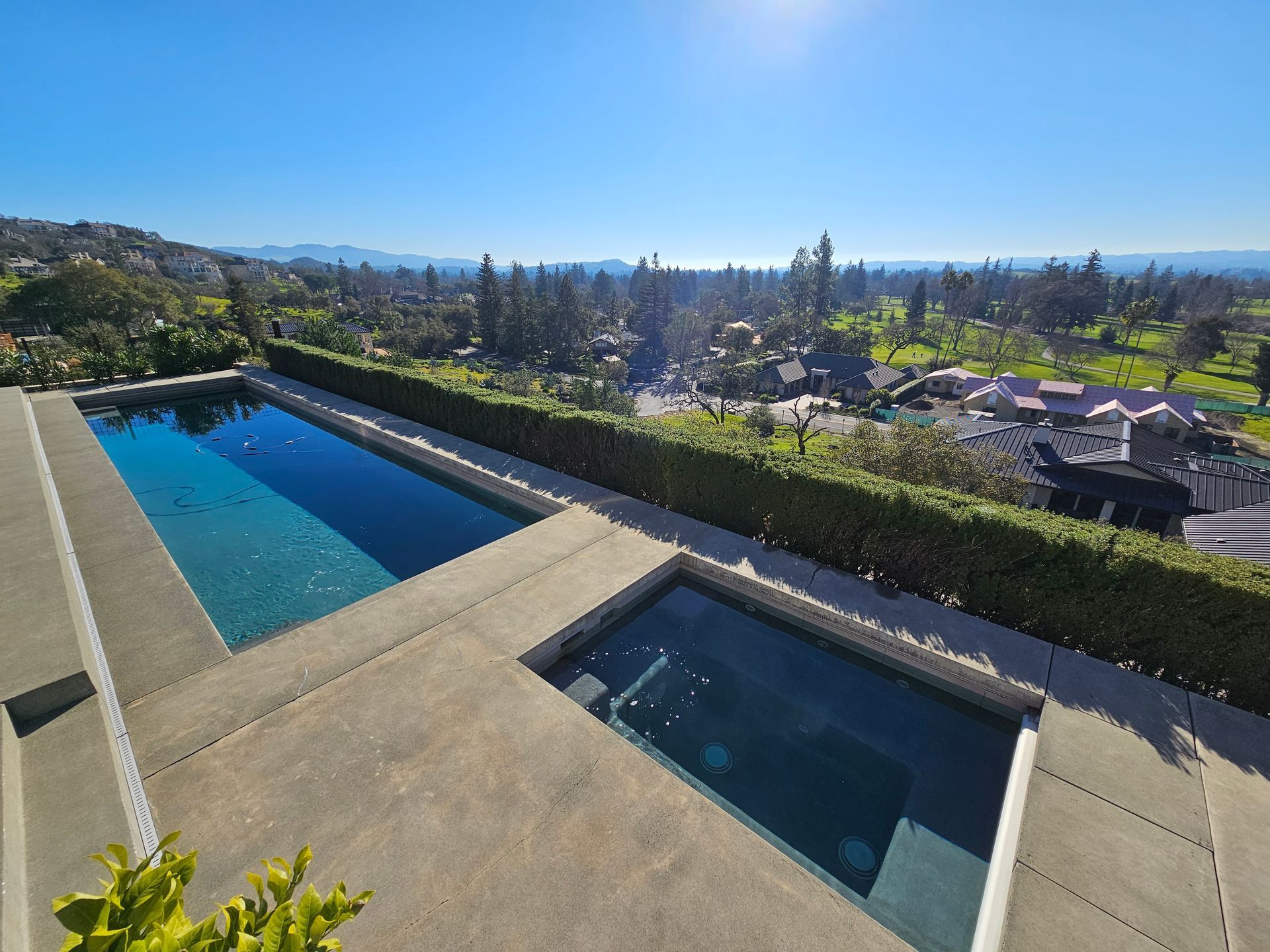 Modern backyard pool and spa overlooking a sunny hillside neighborhood and distant city skyline