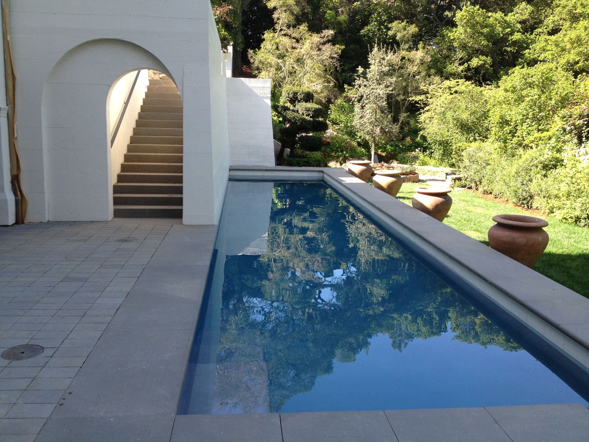 Modern courtyard with a narrow reflecting pool beside white arches and stone steps