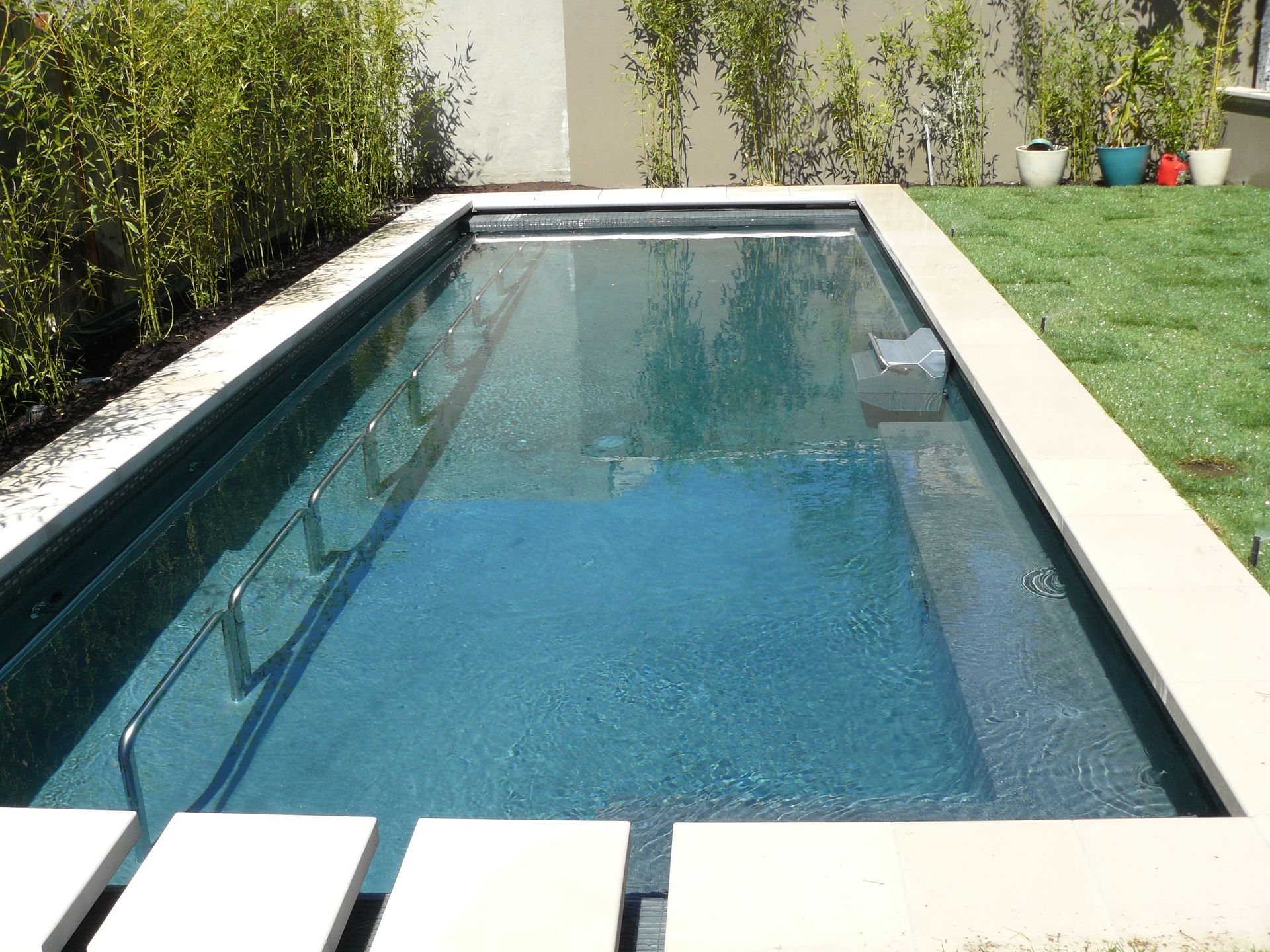 Rectangular backyard swimming pool with blue water beside a white patio and green lawn