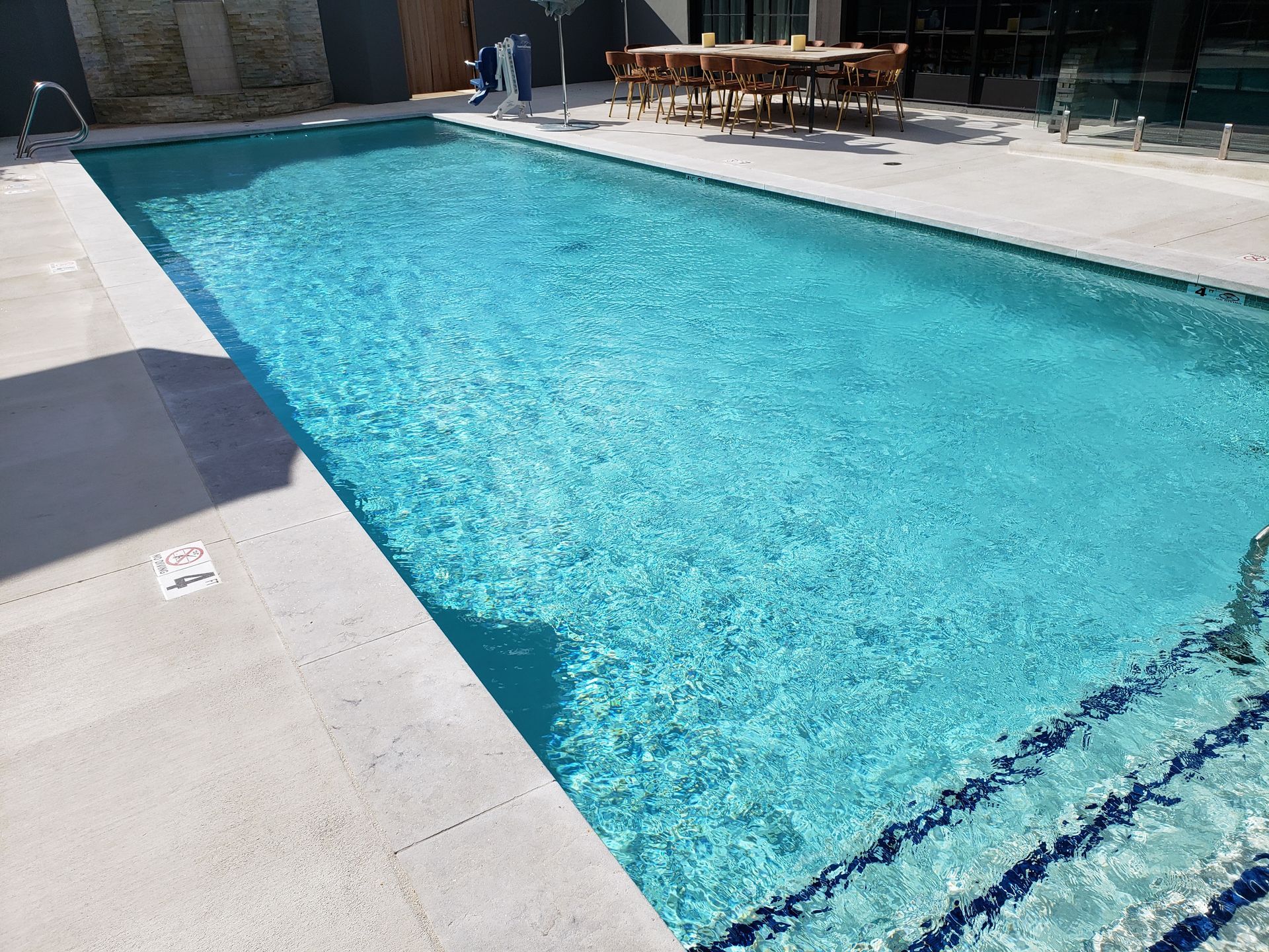Outdoor swimming pool with turquoise water, diving lane markings, and sun loungers on a bright patio.