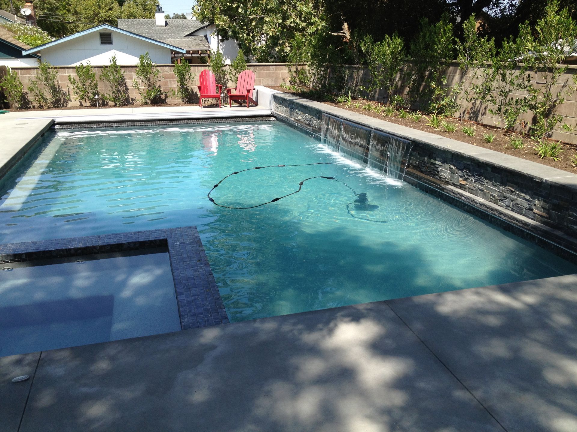 Backyard swimming pool with clear blue water, tiled edge, and patio chairs in the background