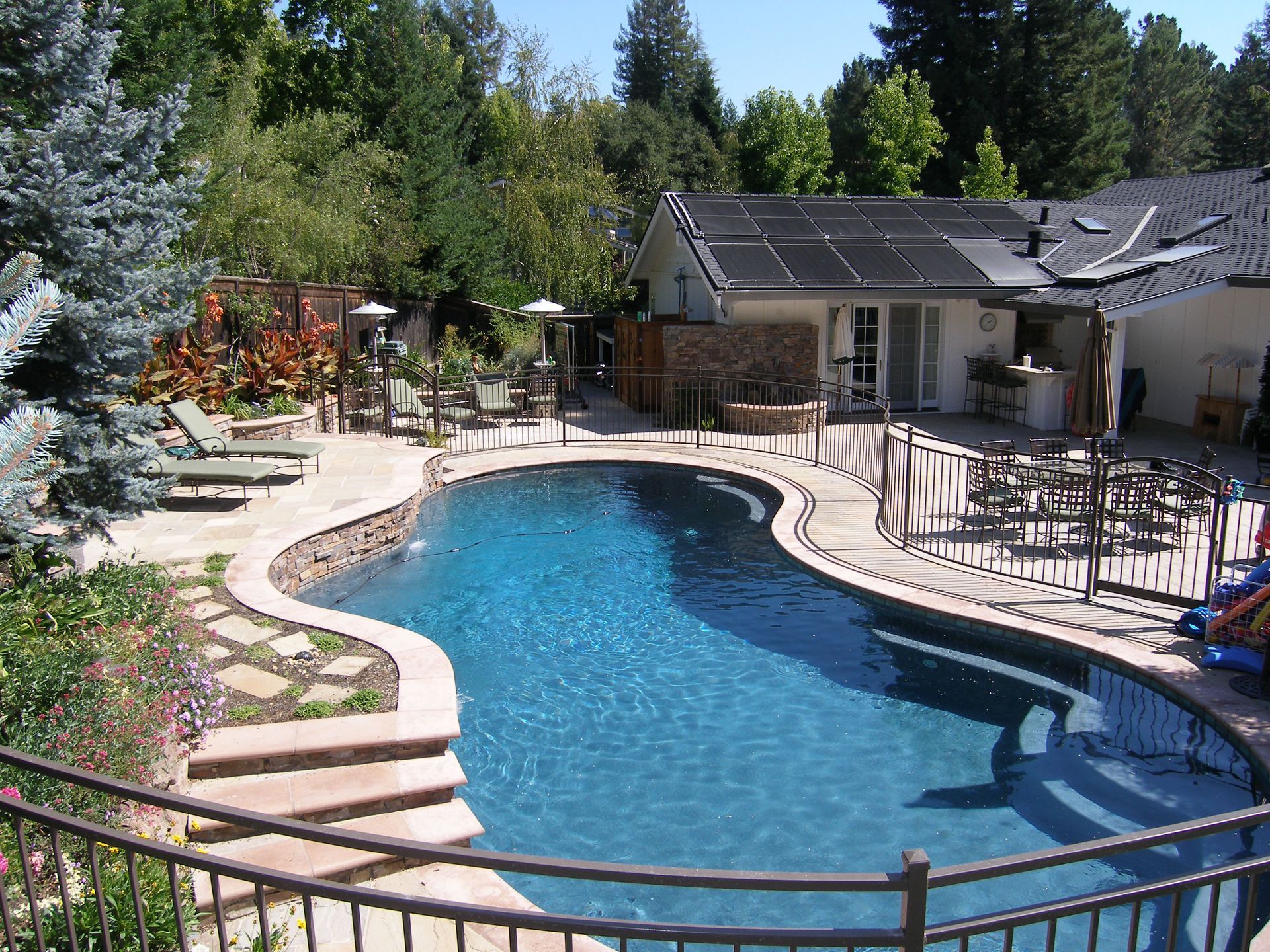 Backyard swimming pool with stone deck, patio chairs, and a house surrounded by trees