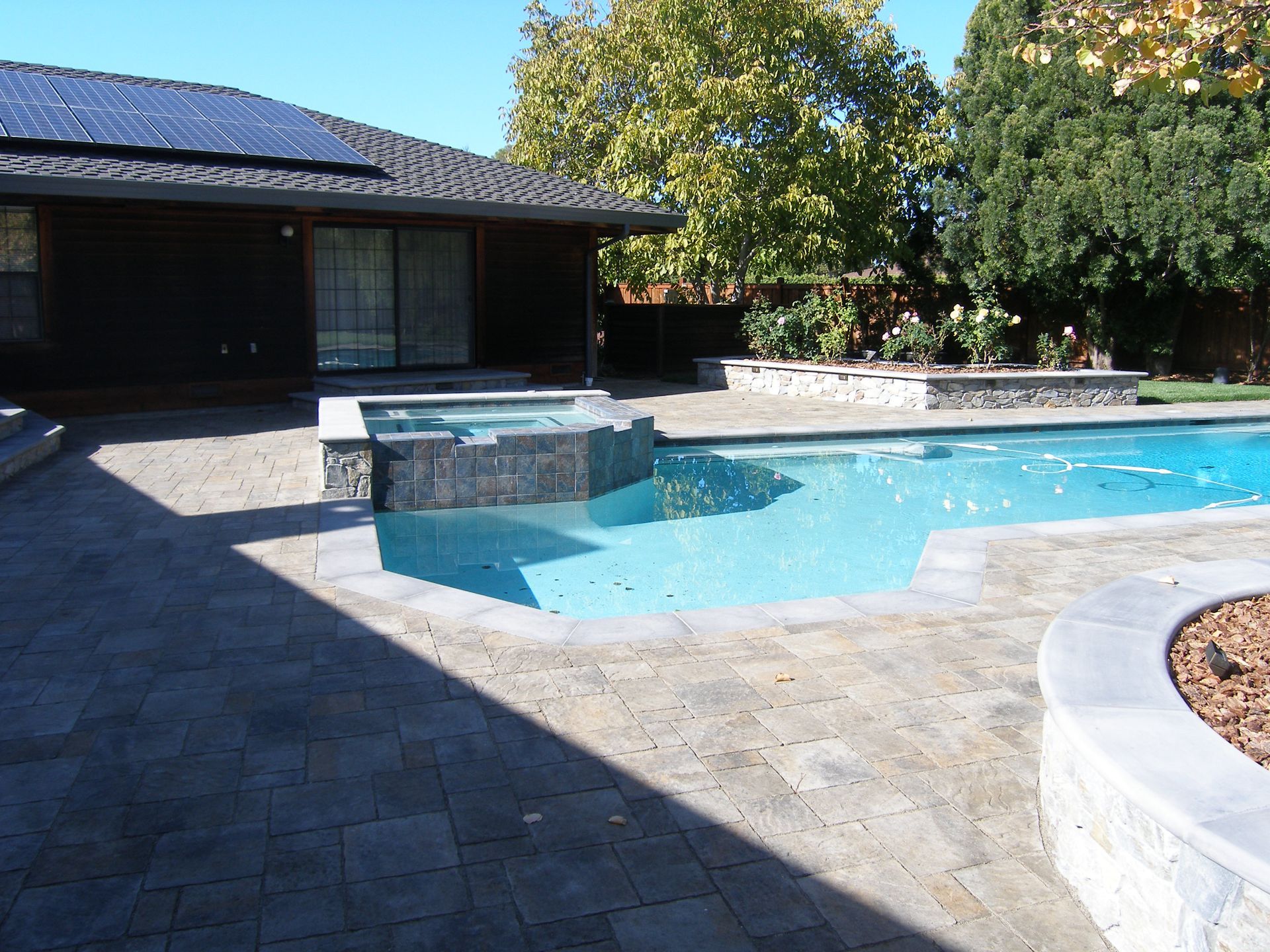 Backyard pool with stone patio, curved steps, and a low stone waterfall beside a house