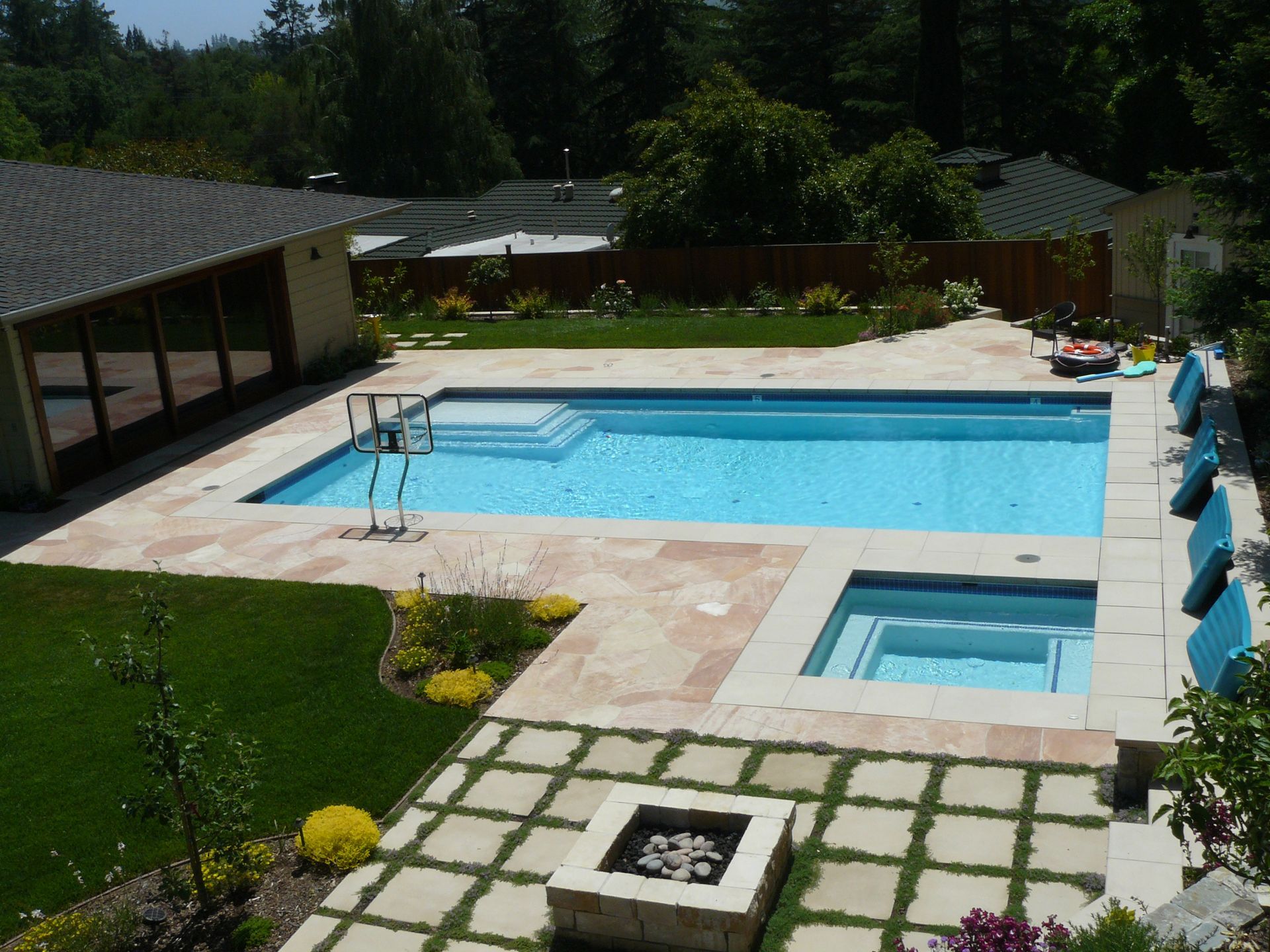 Backyard pool with a hot tub, tiled patio, and lounge chairs beside a lawn.