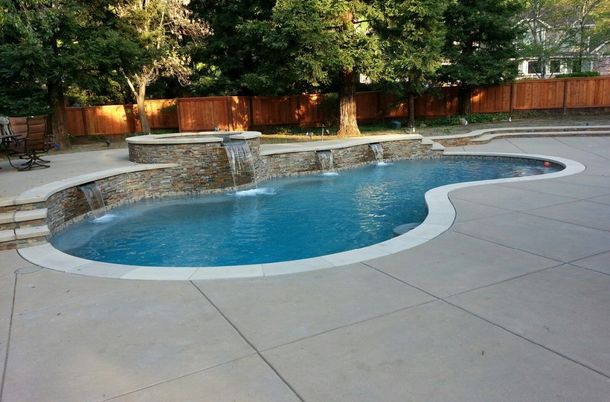 Poolside villa with turquoise water, lounge chairs, and mountain backdrop. Swimming pool with waterfalls and stone accents surrounded by a concrete patio, fence, and trees.
