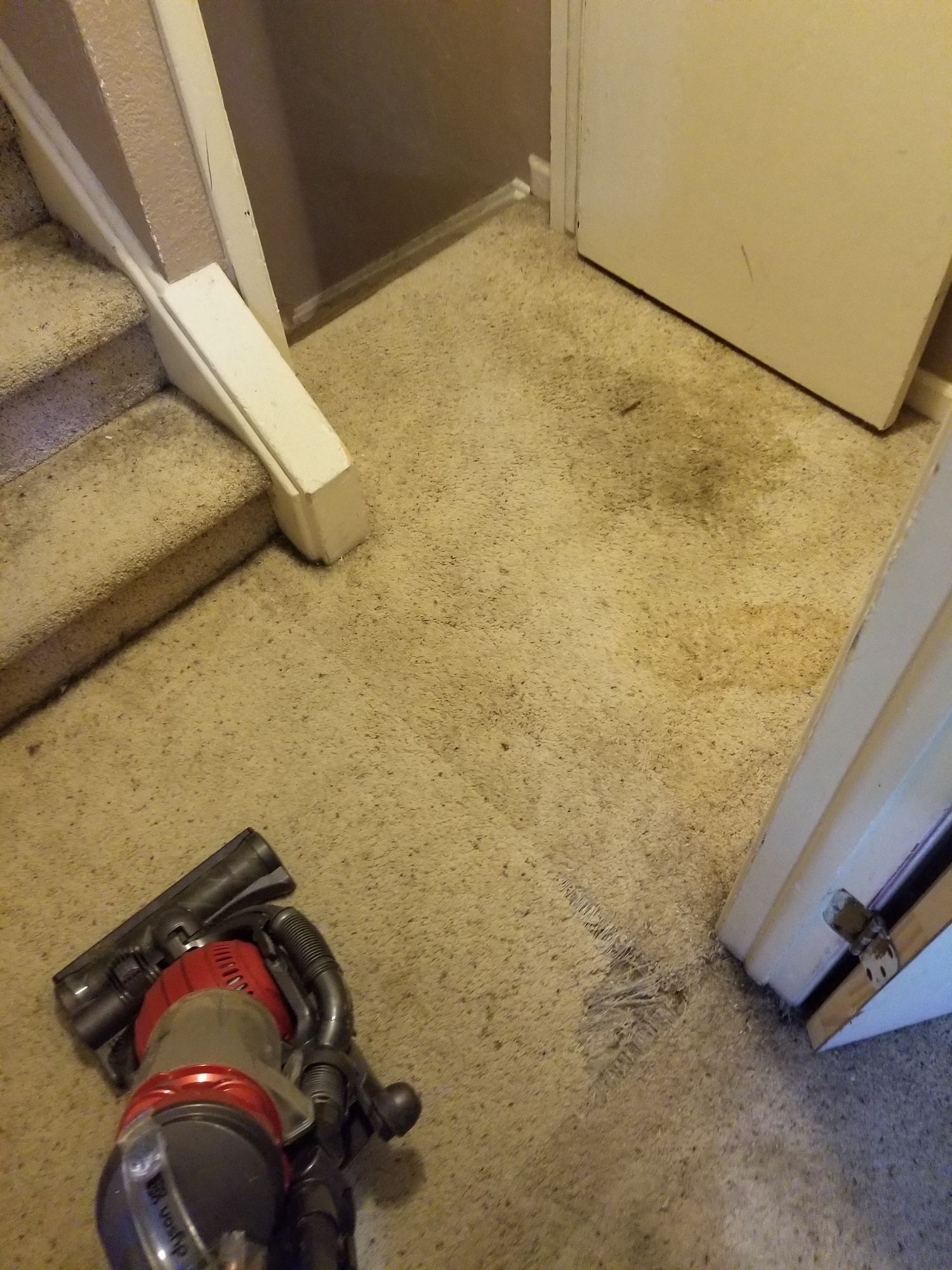 A vacuum cleaner is sitting on a dirty carpet in a room next to stairs.