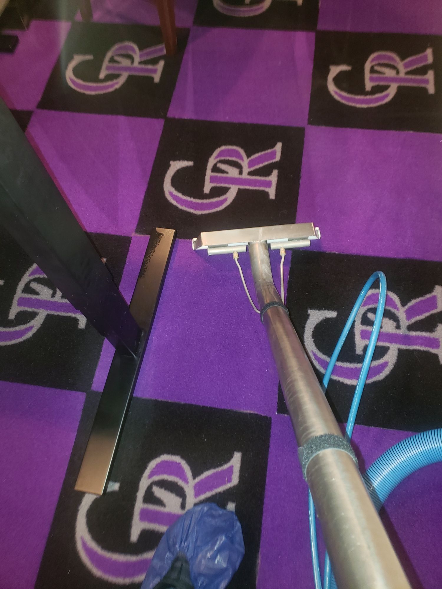 A vacuum cleaner is cleaning a purple and black checkered rug