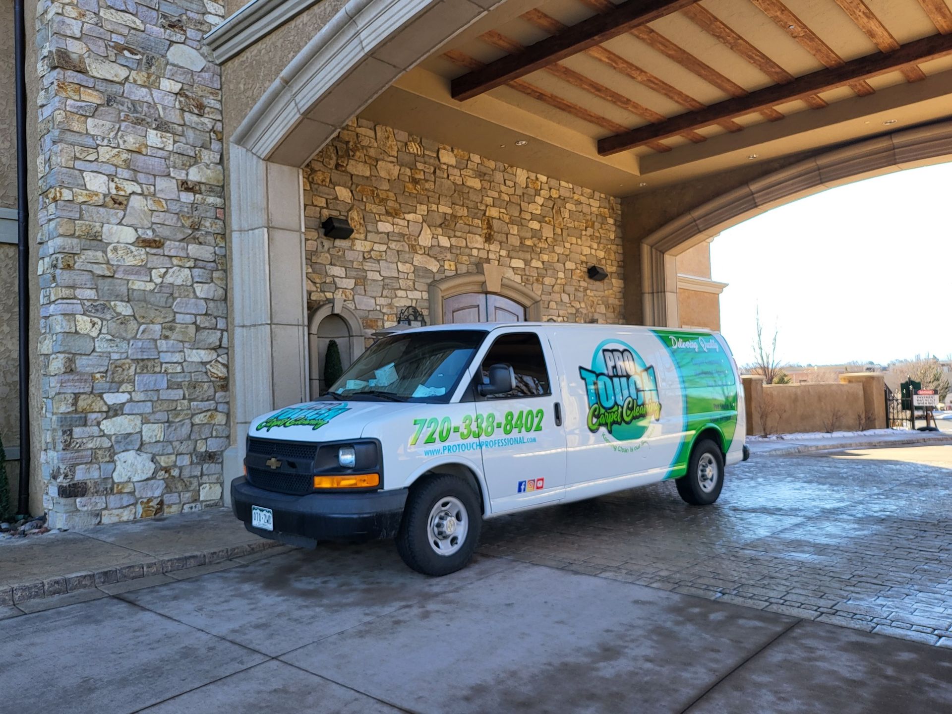 A white van is parked in front of a stone building.
