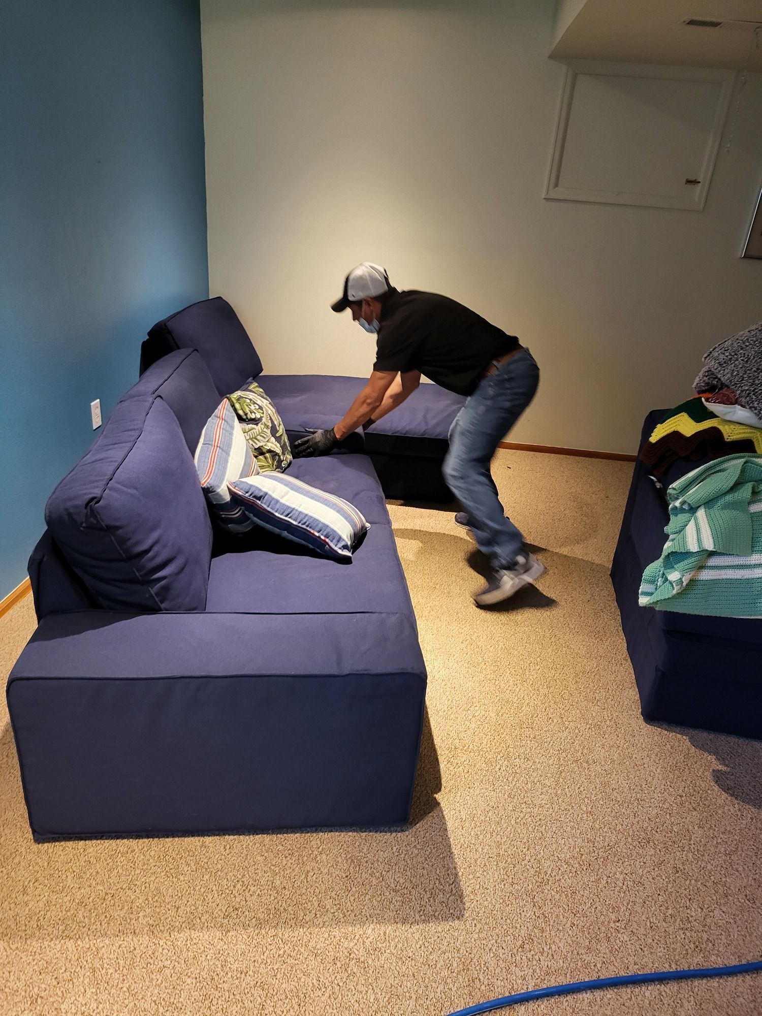 A man is cleaning a blue couch in a living room.