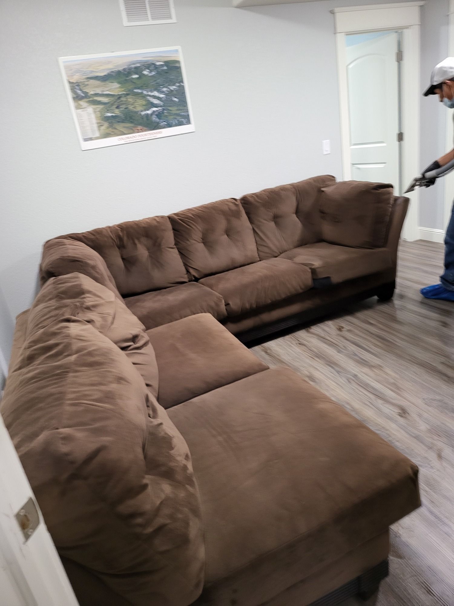 A man is vacuuming a brown sectional couch in a living room.