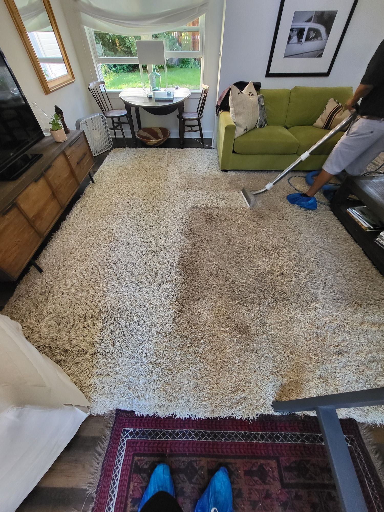 A person is cleaning a rug in a living room with a vacuum cleaner.