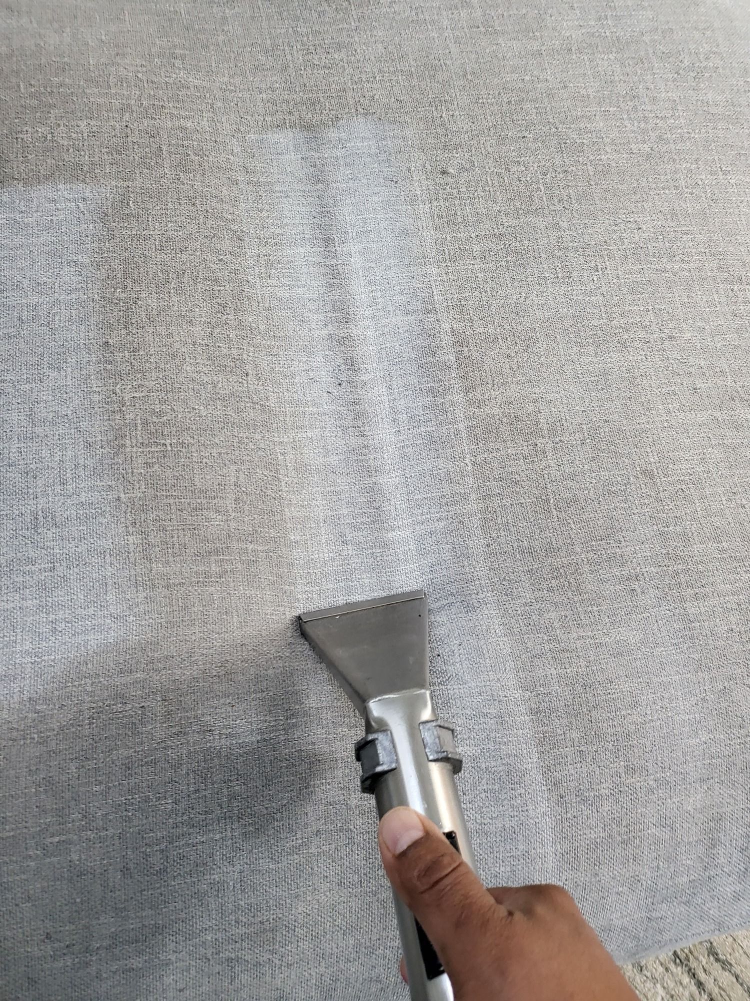 A person is cleaning a couch with a vacuum cleaner.